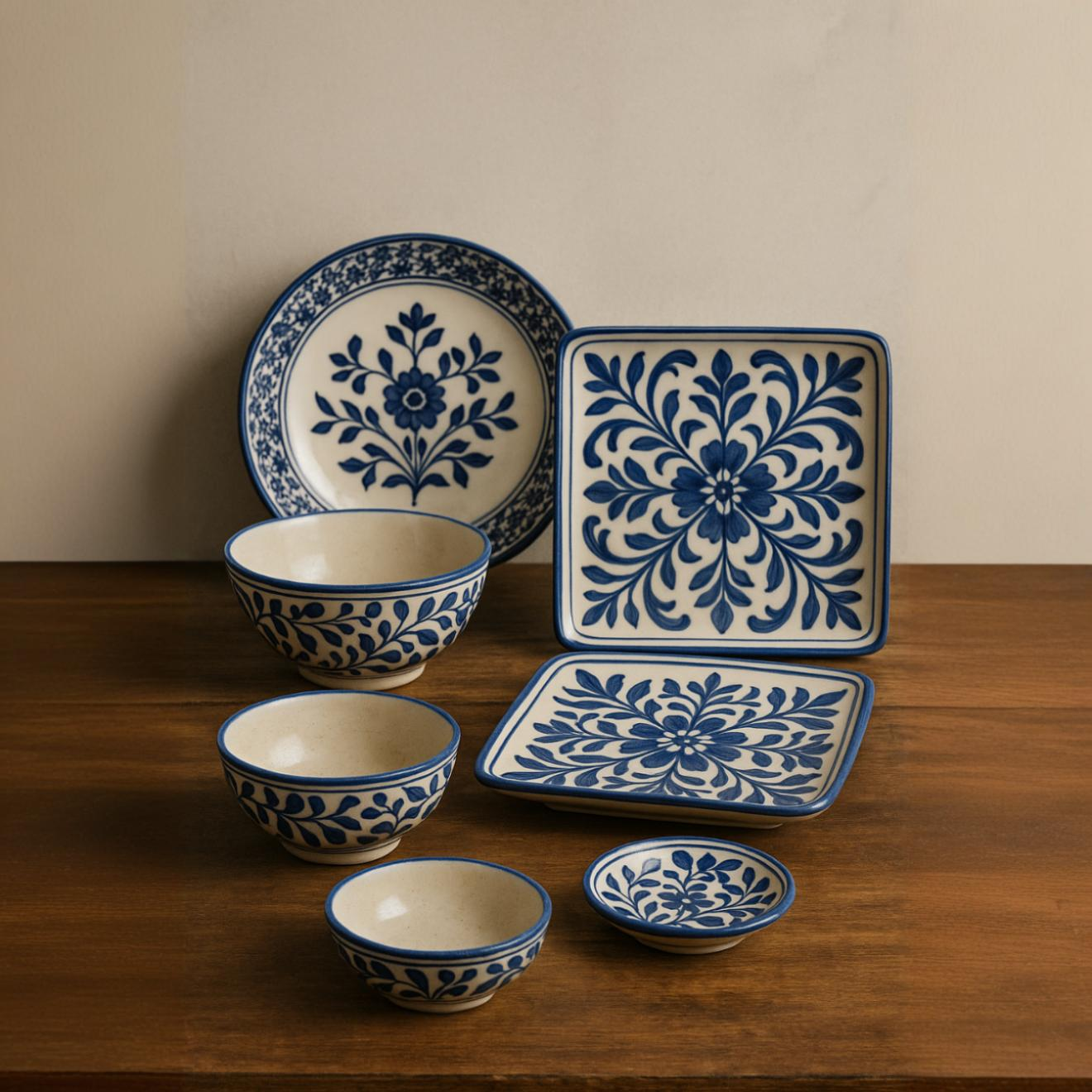 Handcrafted blue and white ceramic bowls and plates featuring traditional floral patterns, displayed on a rustic wooden surface – artisan Multani pottery tableware for dining and decor.
