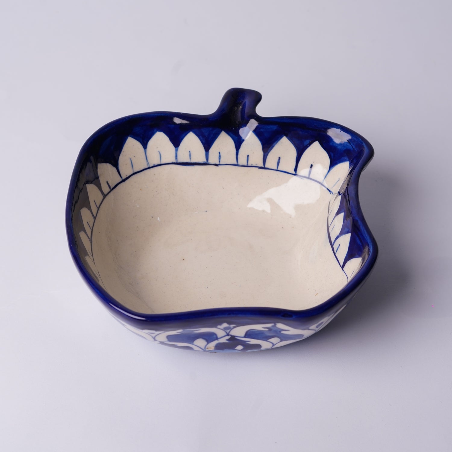 Ceramic apple-shaped multani blue pottery bowl with blue and white design on a light gray background