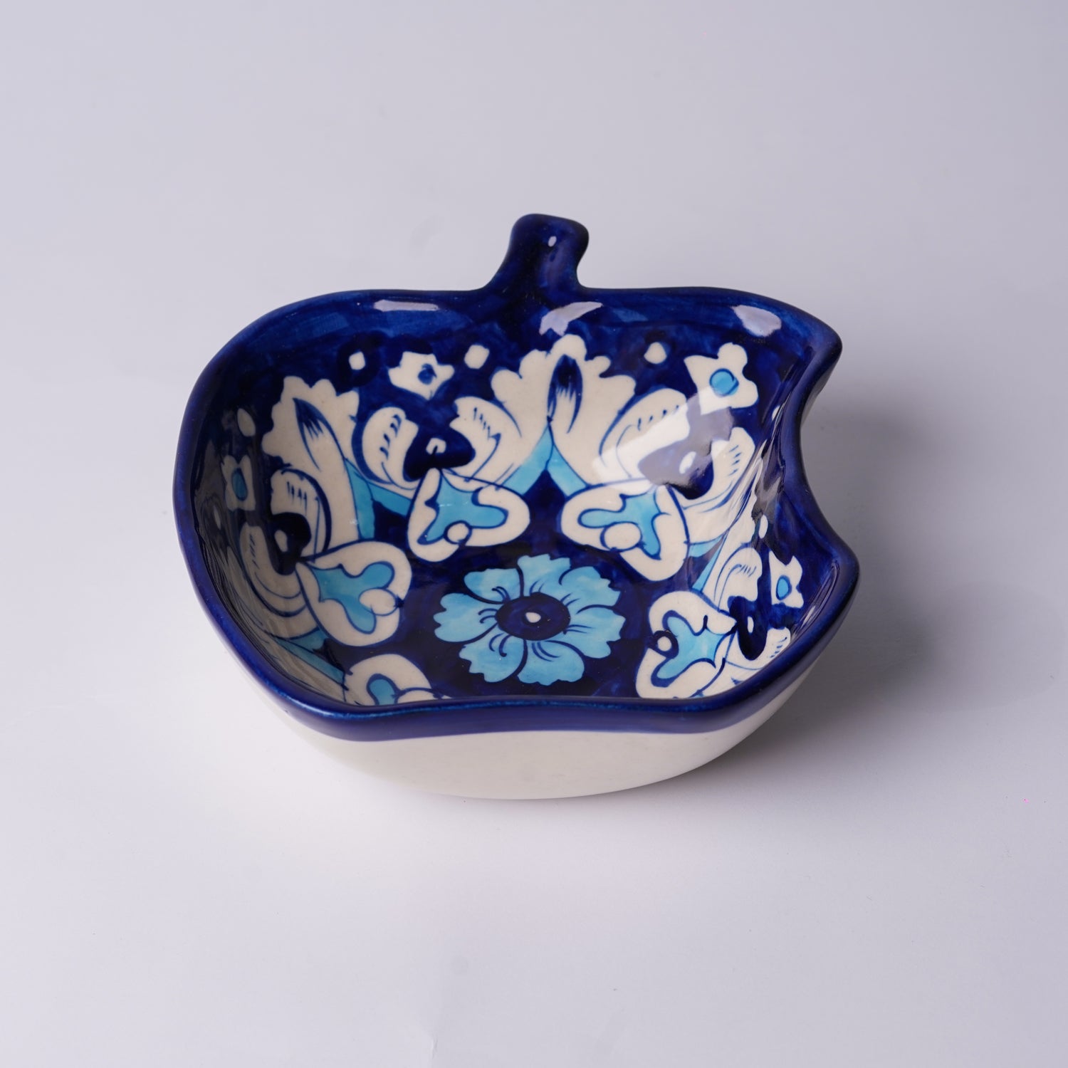 Ceramic apple-shaped multani blue pottery bowl with blue and white floral patterns on a light gray background