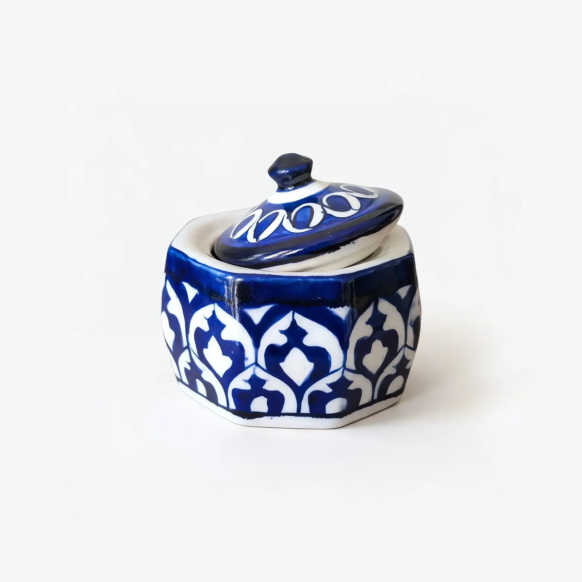 Octagonal blue pottery jewelry box with white arch pattern on cobalt, lid resting at an angle