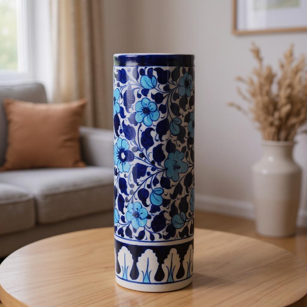 Cylindrical ceramic Multani Blue Pottery vase with blue floral pattern on a wooden table in a living room setting.